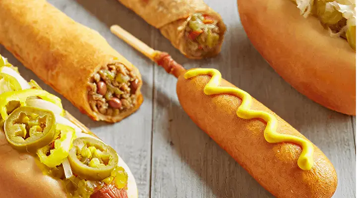 Zoom in on a hotdog with chili and jalapenos, a corndog with mustard, and a taquito.  